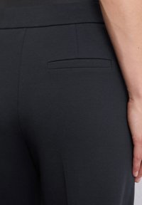 Schwarze Hose mit glatter Stofftextur, einem flachen Gesäßtasche und einer taillierten Passform, die saubere Linien und ein minimales Design betont.