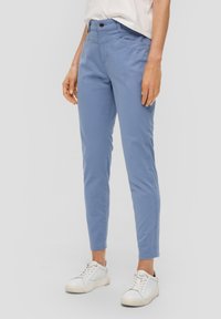 Pantalones de algodón azul claro con un corte ajustado, que cuentan con bolsillos frontales en ángulo y cierre de botón. Combinados con zapatillas blancas.