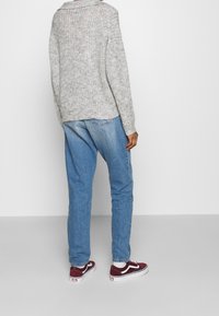 Pullover grigio chiaro a maglia, taglio morbido, con colletto casual, abbinato a jeans in denim blu e sneakers bordeaux con dettagli bianchi.