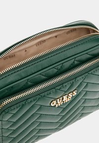 Borsa a tracolla trapuntata verde con hardware dorato, dotata di due scomparti con zip e logo impresso sulla parte anteriore. Finitura in pelle liscia.