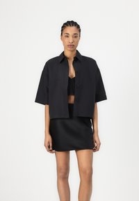 Black cropped button-up shirt with short sleeves, paired with a matching fitted black skirt. Smooth fabric, minimal design, no patterns or accents.