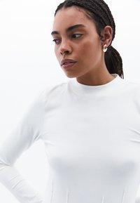 Weißes Langarmoberteil mit hohem Kragen, präsentiert sich in einem figurbetonten Design und weichem Material, akzentuiert durch dezente Nahtdetails.