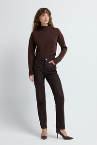 Brun stickad tröja med hög krage, tillsammans med mörkbruna texturerade byxor. Modellen bär eleganta bruna högklackade skor.