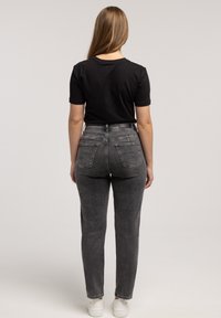 Czarna koszulka na krótki rękaw z zaokrąglonym dekoltem, zestawiona z wysokim stanem szarymi dżinsami o prostych nogawkach. Tkanina wydaje się miękka, z minimalnymi zdobieniami.