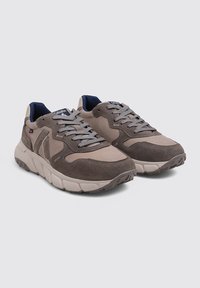 Une paire de baskets à lacets marron et beige avec des semelles blanches épaisses et un doublure intérieure bleu marine sur un fond uni.