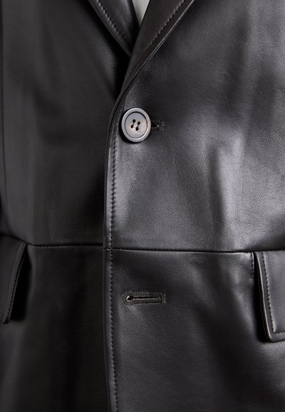 Close-up of a black leather jacket buttoned at the chest with visible stitching and a buttonhole below.