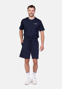 T-shirt en coton bleu marine avec un logo, associé à un short assorti. Des chaussettes blanches avec un accent et des baskets blanches complètent la tenue.