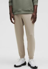 Beige sweatpants i en tapered pasform med en glat tekstur, parret med hvide sneakers med en sort spraglet sål.