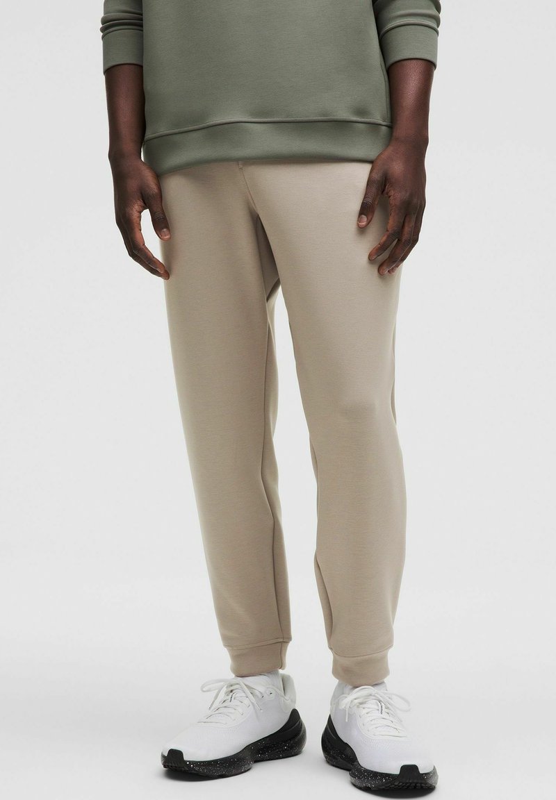 Beige sweatpants i en tapered pasform med en glat tekstur, parret med hvide sneakers med en sort spraglet sål.