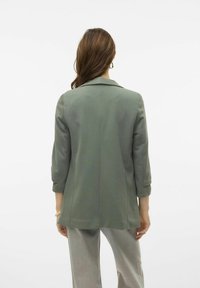 Olijfgroene blazer met een gestructureerd ontwerp, notch-revers, driekwartmouwen en een getailleerde pasvorm. Gladde textuur, minimalistische stijl.