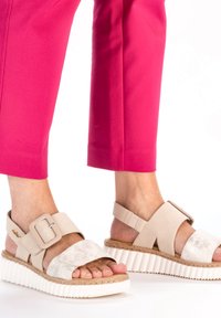 Beige plattform sandaler med texturerad fotbädd, breda remmar, stor spänne och vit ribbad sula, i kombination med ljusrosa capribyxor.