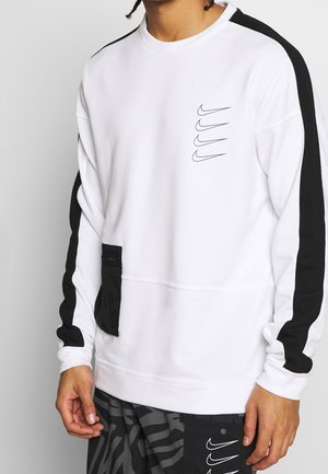 Person iført hvid sweatshirt med sorte striber på ærmerne og fire sorte Nike Swoosh-logoer på brystet samt en sort lomme.