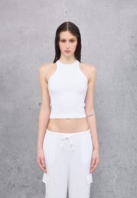 Weißes, gekürztes Halstopp aus geripptem Stoff, kombiniert mit leichten, hosen mit Kordelzug an der Taille und seitlichen Taschen. Sanfte Textur, minimalistisches Design.
