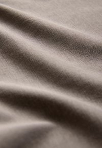Bavlnená látka v svetlo hnedej farbe s hladkým, textúrovaným povrchom, ktorý má jemné záhyby a vrásky vytvárajúce hĺbku.
