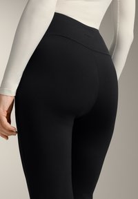 Black high-waisted leggings with a smooth texture and a seamless design, featuring a subtle logo and a form-fitting shape.