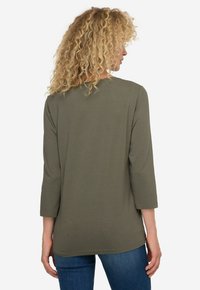 Oliwkowa bluzka z długim rękawem, okrągłym dekoltem i luźnym krojem, charakteryzująca się gładką fakturą i lekko zaokrąglonym dołem.