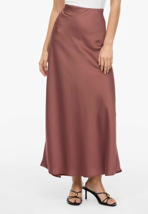 Femme portant une jupe midi en satin couleur rouille taille haute et des sandales à talons noirs avec des lanières fines et des accents dorés.