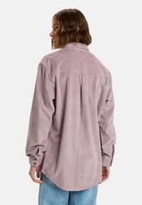 Lange mouwen shirt van zachte, lichte paarse corduroy met een kraag, rugplooi en knoopmanchetten, gecombineerd met blauwe jeans.