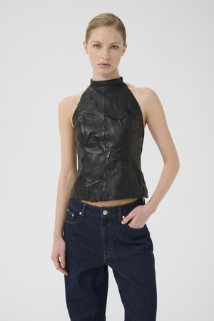 Schwarzes Leder-Haltertop mit texturiertem Finish und vorderer Nahtdetail, kombiniert mit dunkelblauen, hoch geschnittenen Jeans.