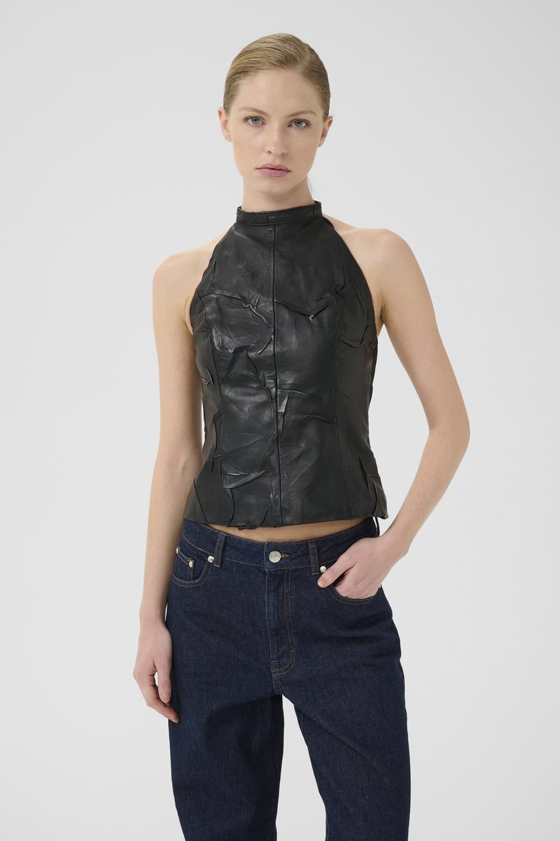 Svart skinn halterneck-top med en teksturert overflate og front-søm detaljer, kombinert med mørkeblå, høy-midje denimjeans.