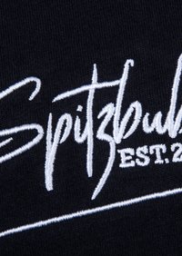 Schwarzer Stoff mit weiß gesticktem Text "Spitzbuhl EST. 20", mit glatter Textur und fett fließender Schrift.