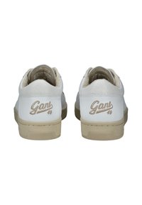 Zapatillas de cuero blanco con un talón de ante gris claro. Presentan acentos beige, suelas texturizadas y un logo dorado "Gant 49" en la parte trasera.
