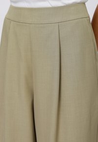 Světlé khaki kalhoty s širokými nohavicemi, sklady, hladkým povrchem a vysokým pasem. Zúžený design bez viditelného kovového zapínání nebo vzorů.