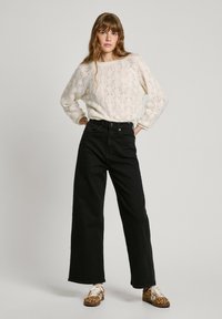 Stickad krämfärgad tröja med strukturerat mönster, högmidjade svarta vida jeans och bruna sneakers med leopardmönster och vita snören.