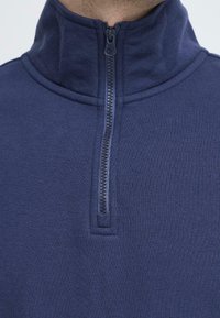 Pullover blu navy a mezza zip realizzato in tessuto morbido con una superficie liscia, caratterizzato da una cerniera robusta e un design colletto alto.