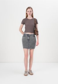 Šedý žebrovaný crop top s krátkým rukávem, zkombinovaný se šedou džínovou mini sukní a béžovými šněrovacími botami. Hnědá kabelka přes rameno jako akcent.