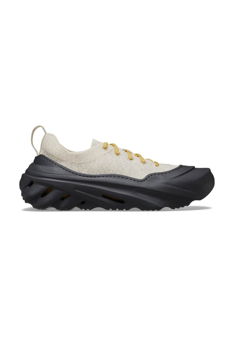 Scarpe da ginnastica grigio chiaro con una tomaia testurizzata e suola in gomma nera. Presentano lacci gialli e un design arrotondato e aerodinamico.