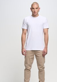 Witte t-shirt met korte mouwen en een ronde halslijn, gecombineerd met beige slim-fit broeken. Smooth stof met minimale details, aansluitende silhouet.
