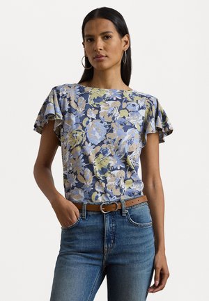 Haut à manches courtes fleuri en bleu, jaune et beige, avec un col rond et des manches volantes, associé à un jean bleu et une ceinture marron.