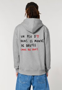 Felpa grigia con cappuccio regolabile, caratterizzata da testo nero e rosso sulla schiena. Il materiale è morbido con una texture in pile e polsini a coste.