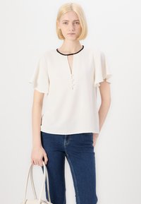 Blusa bianca con maniche corte a volant, scollatura a V profonda e tre bottoni sul davanti, con rifiniture nere. Design casual.