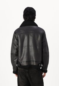 Schwarze Lederbomberjacke mit Schaffellkragen, mit einer cropped Design, seitlichen Schnallen und kontrastierendem Felltextur an den Bündchen.