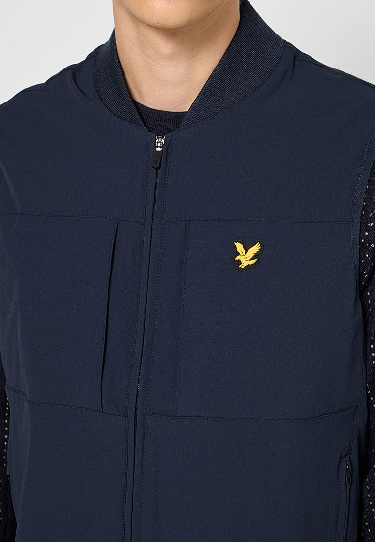 Veste sans manches bleu marine avec fermeture éclair à l'avant, en tissu texturé, et un petit logo d'oiseau jaune sur la poche poitrine.