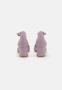 Talons en cuir lilas avec un dos fermé, une bride de cheville et un talon carré. Texture lisse, bout rond et semelle de couleur naturelle.