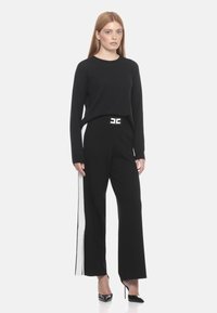 Maglione nero a maniche lunghe abbinato a pantaloni larghi neri con strisce laterali bianche e una cintura decorativa in bianco e nero. Tacchi neri.