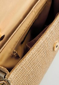 Woven straw handbag with a beige fabric lining, featuring a zippered pocket, snap closure, and gold accents. Soft texture and structured shape.