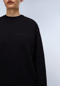 Černá mikina s kulatým výstřihem, na hrudi s embosovaným logem "NAPAPURI", vyrobena z měkké texturované tkaniny.