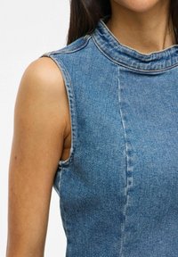 Top sans manches en denim avec un col montant, de couleur bleu clair, aux lignes épurées et présentant des détails de couture visibles le long des coutures.