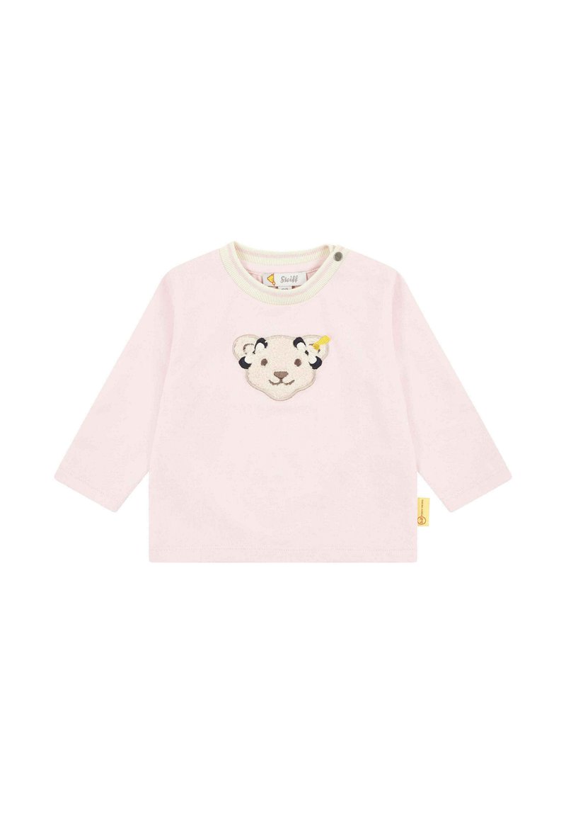 Helles, pinkes Langarmshirt mit Rundhalsausschnitt, das in der Mitte ein weiches, gesticktes Design eines Löwenkopfes zeigt und ein gelbes Etikett an der Seite hat.