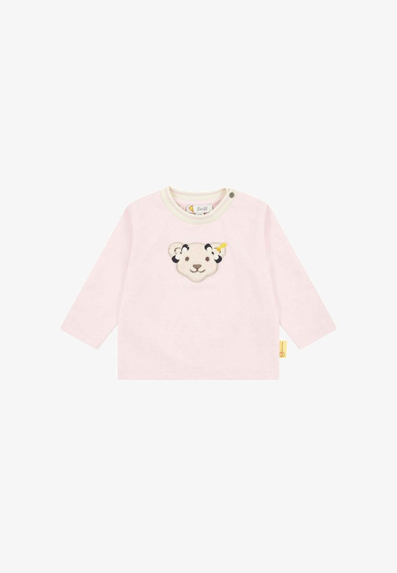 Helles, pinkes Langarmshirt mit Rundhalsausschnitt, das in der Mitte ein weiches, gesticktes Design eines Löwenkopfes zeigt und ein gelbes Etikett an der Seite hat.