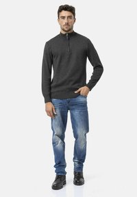 Donkergrijs gebreid sweater met halve rits, lange mouwen, geribbelde boorden en onderrand, gecombineerd met lichtblauwe jeans en zwarte veterschoenen.