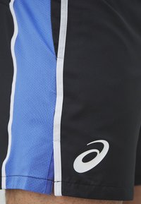 Shorts de sport noirs et bleus avec un tissu texturé, des rayures blanches sur les côtés et un logo Asics en blanc au bas.