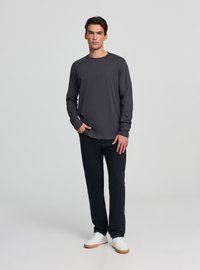 Długi rękaw szarej koszulki wykonanej z miękkiego materiału, zestawionej z czarnymi spodniami i białymi trampkami. Koszulka ma okrągły dekolt i luźny krój.