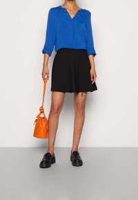 Niebieska bluzka w serek z podwiniętymi rękawami, czarna rozkloszowana spódnica, czarne masywne loafersy oraz pomarańczowa torba typu bucket. Gładki materiał, casualowy styl.