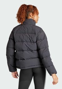 Czarna kurtka puchowa z wysokim kołnierzem, pikowanym wzorem i długimi rękawami. Miękka, gładka tekstura z poziomymi szwami i luźnym krojem.