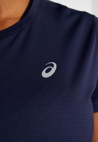 Maglietta sportiva blu navy con tessuto strutturato, caratterizzata da un logo argentato sul petto. Scollatura tonda e maniche corte.